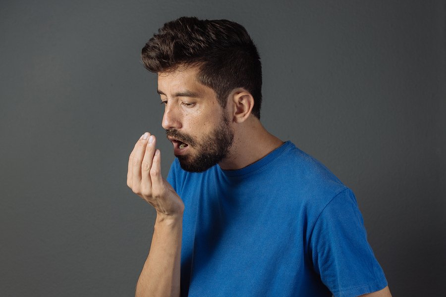 Bad breath. Halitosis concept. Young man checking his breath with his hand.