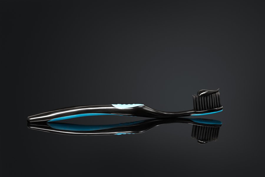 Toothbrush with black charcoal toothpaste on glossy reflective background