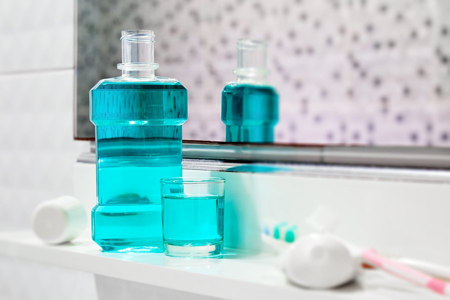 Oral cleanser for good oral health Bottle and glass of mouthwash on bath shelf with blurred toothbrush and toothpaste in foreground