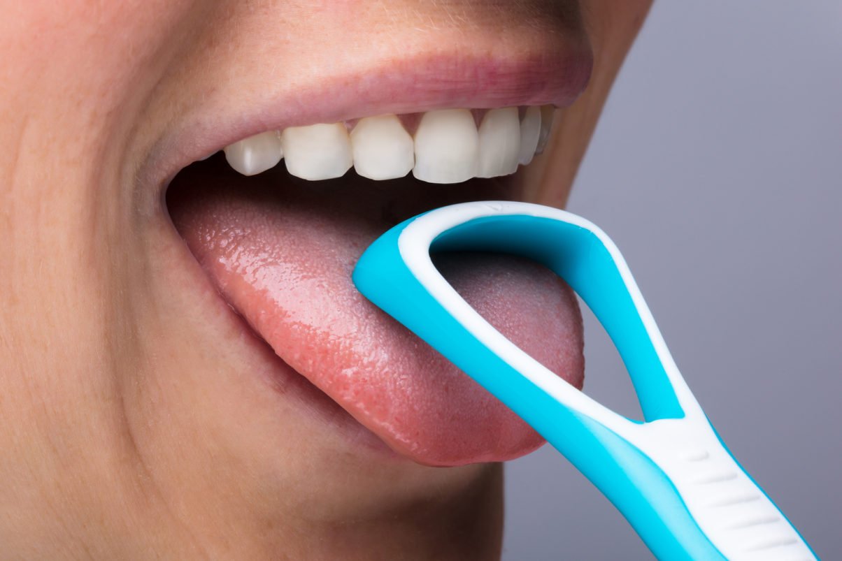 Close-up Of Young Woman Cleaning Tongue With Cleaner