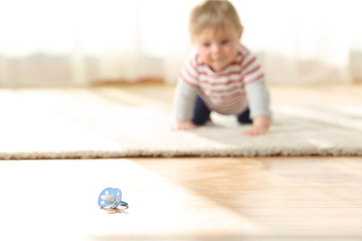 baby crawling towards a pacifier on the floor at home
