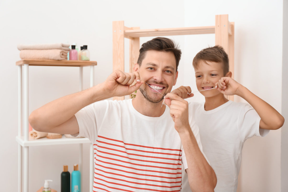 Father and son flossing their teeth in a bathroom.
