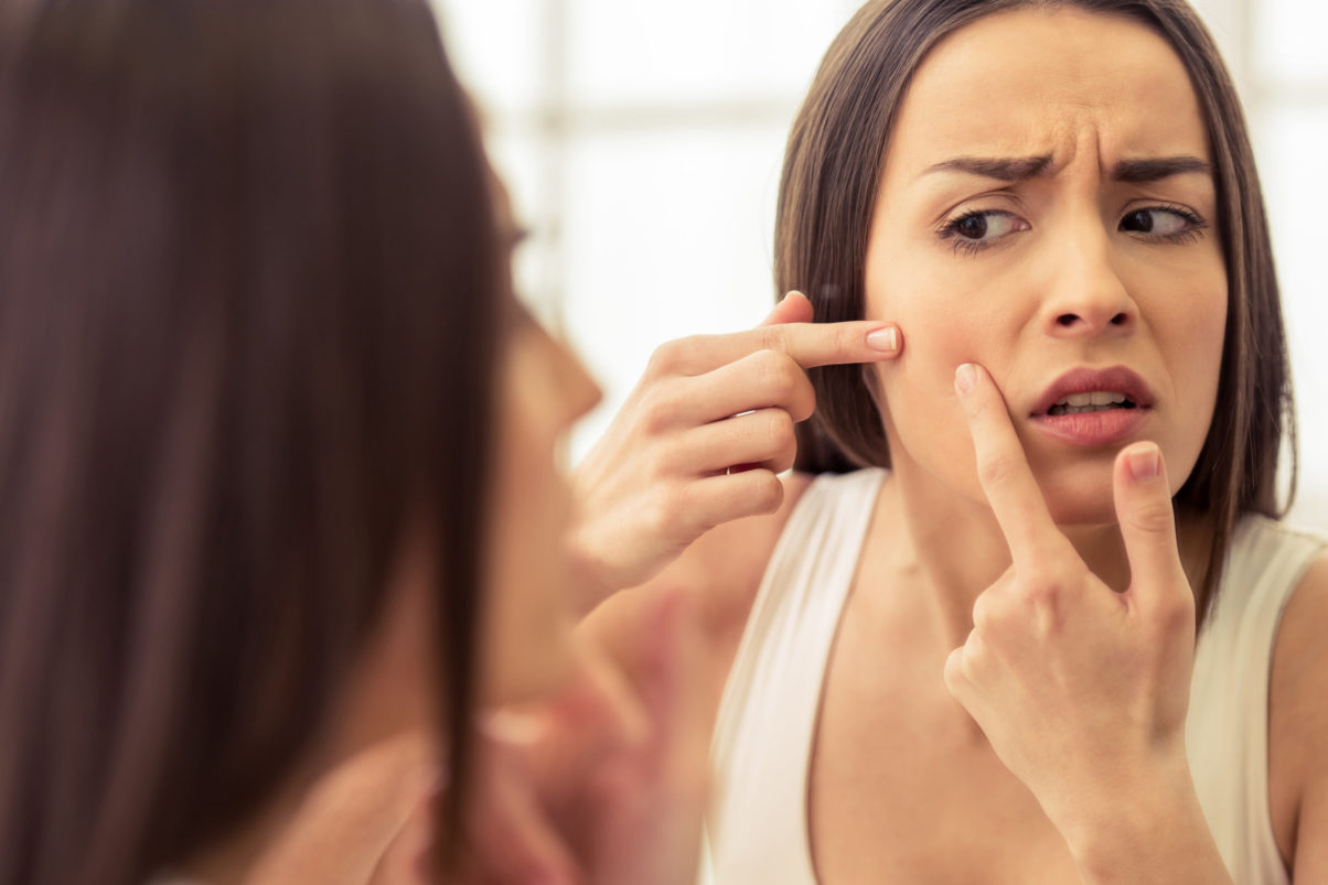 A woman examining her acne from poor oral health looking in the mirror.