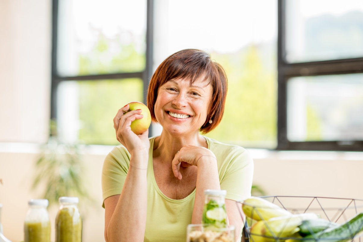 A woman with a healthy mouth smiling and holding an apple