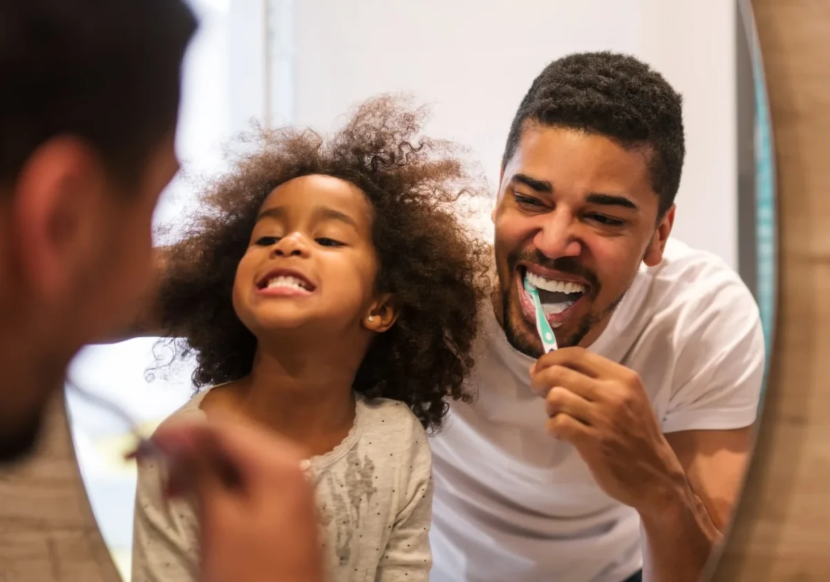 Image of African American girl brushing teeth with her father.