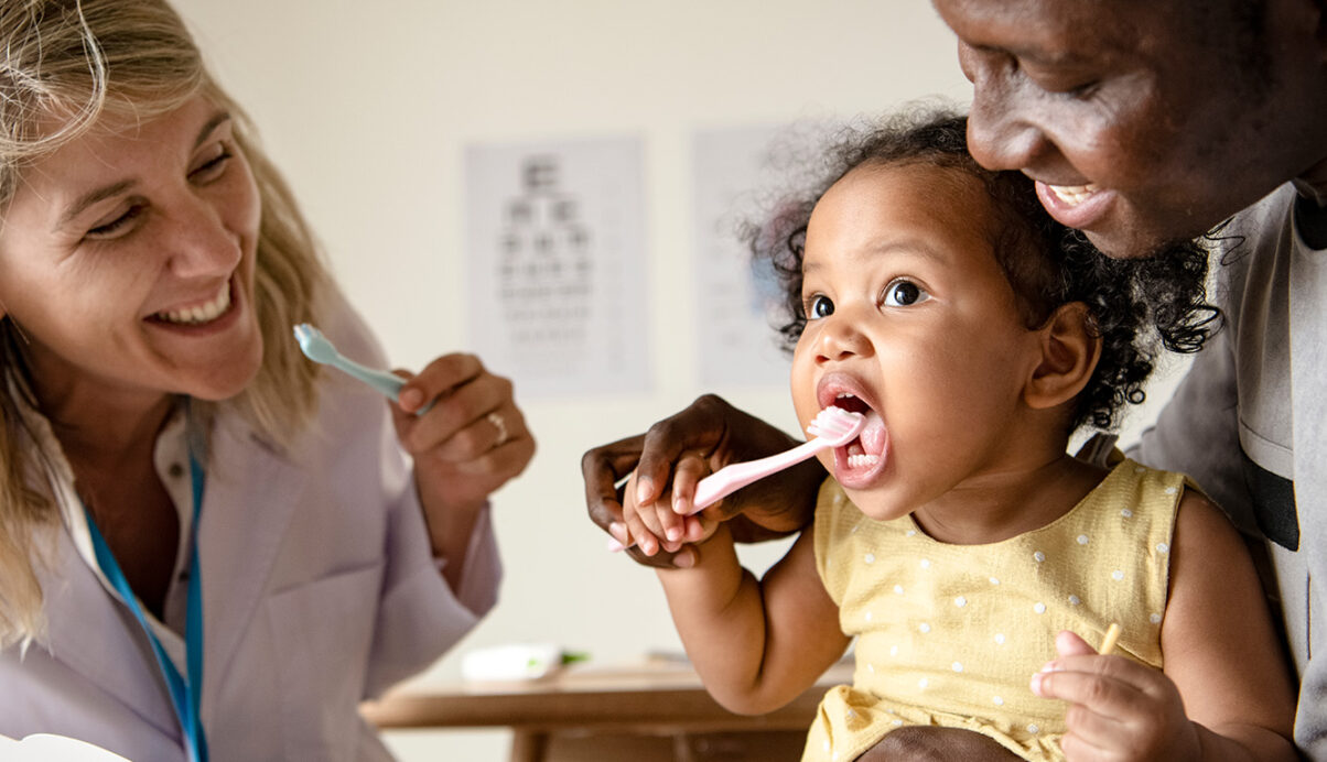 parent helping child brush teeth while dentist watches