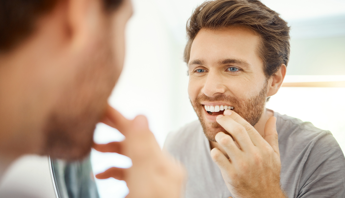 man looking into mirror and touching his teeth