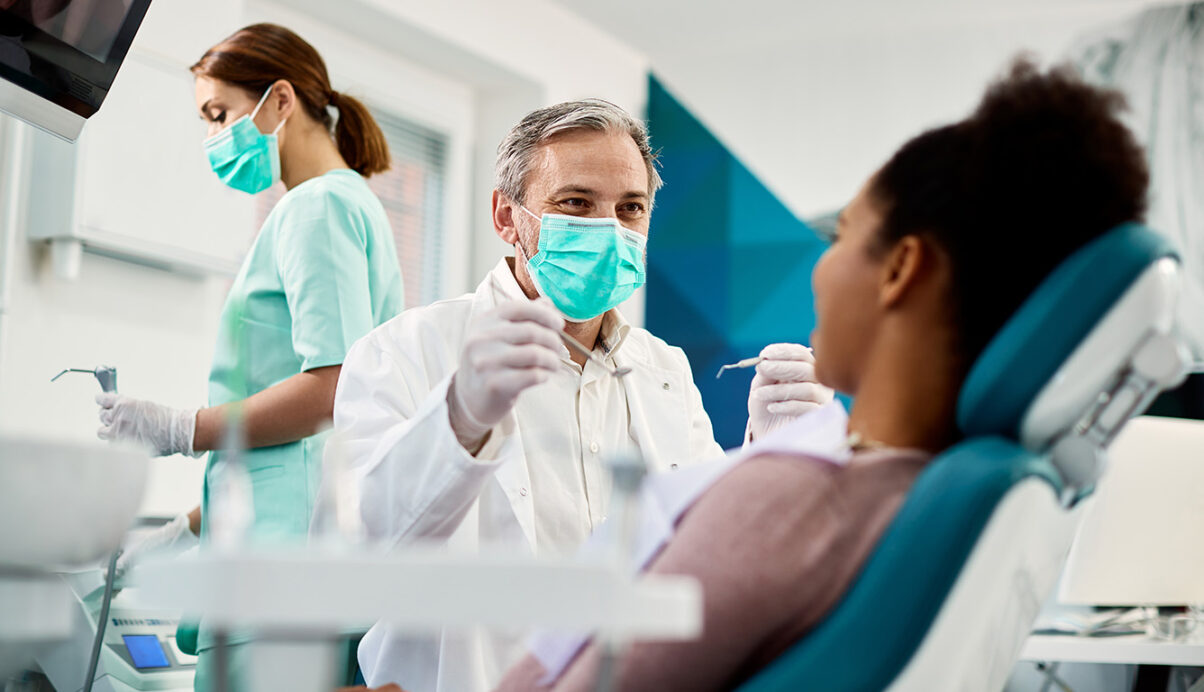 female patient in dental chair with dentist moving dental tool towards her mouth