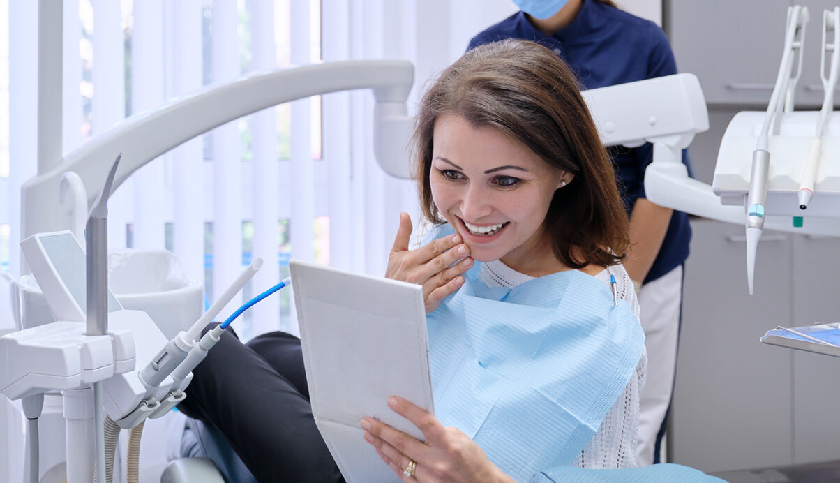woman in dentist office admiring smile in hand mirror