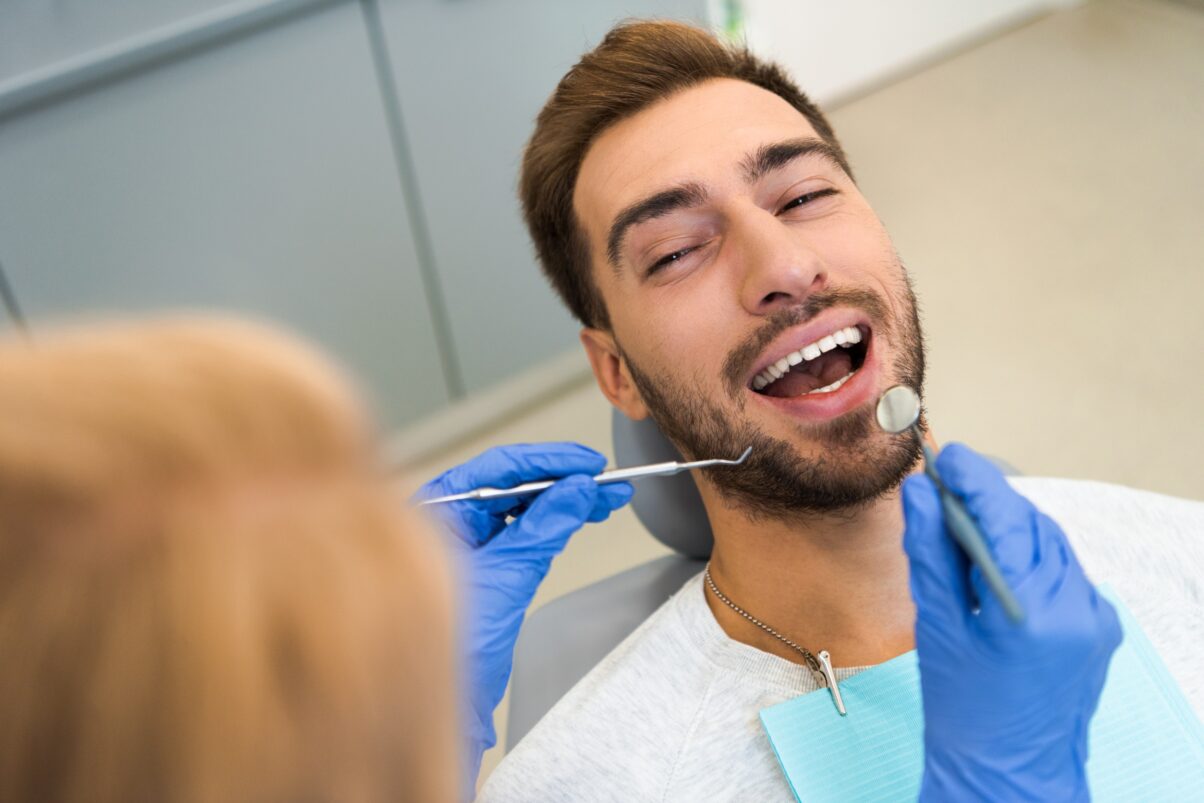 Young male dental patient with dark hair and beard, opening his mouth.