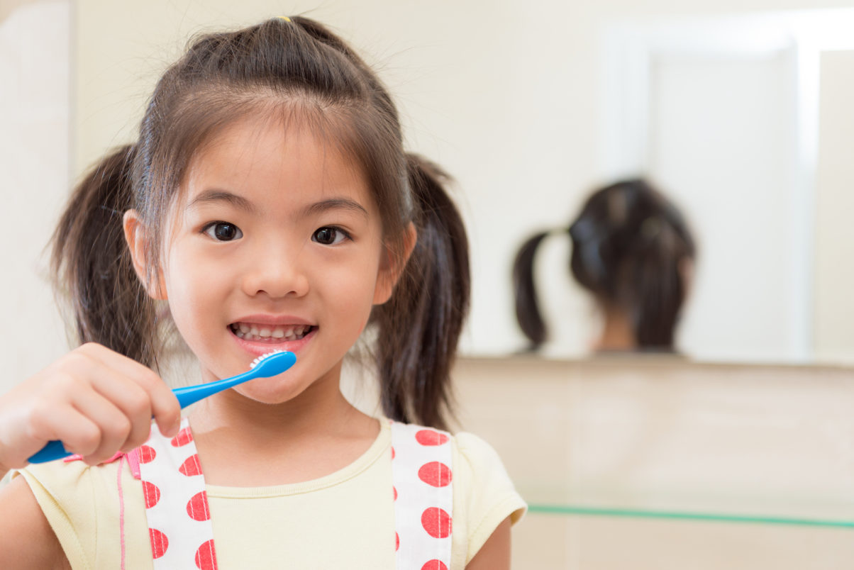 young girl holding children toothbrush standing in front of bathroom mirror and face to camera ready cleaning teeth at home.
