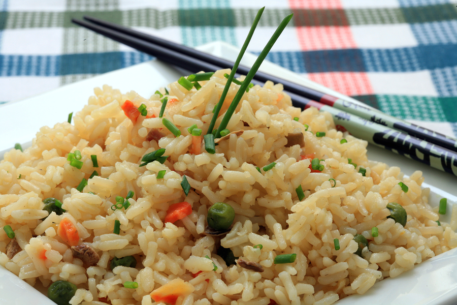 A plate of oriental fried rice with vegetables and chopsticks
