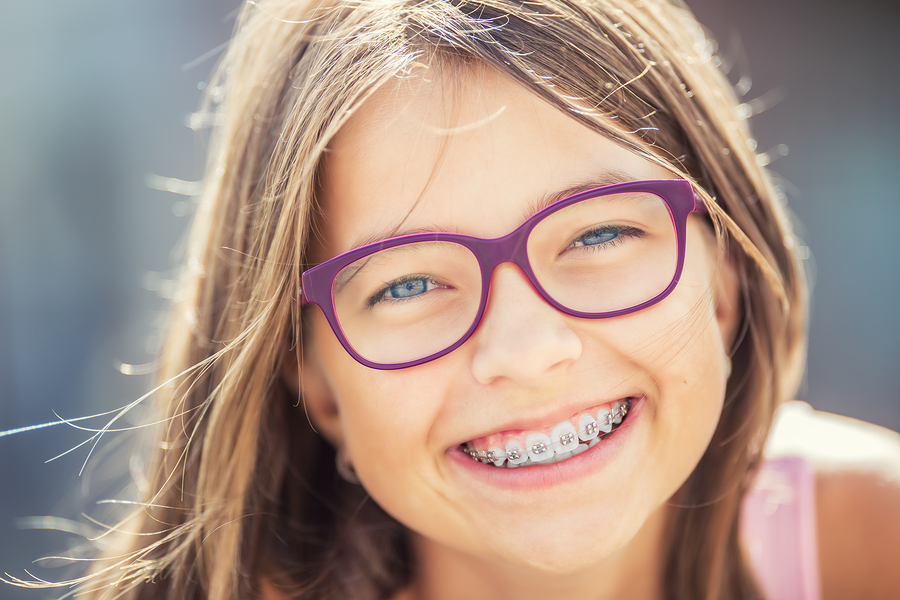 Happy smiling girl with dental braces and glasses. Young cute caucasian blond girl wearing teeth braces and glasses.