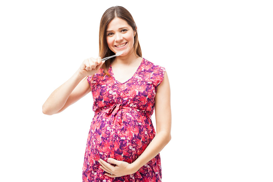 Pretty young Hispanic pregnant woman holding a toothbrush and taking care of her teeth during pregnancy