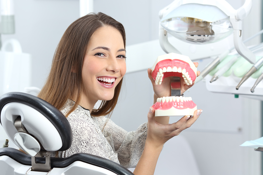 Portrait of a dentist patient smiling with perfect teeth after whitening treatment and holding a plastic denture in a box