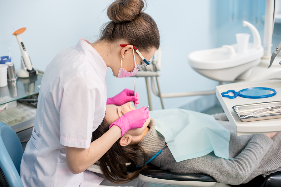 Female dentist with dental tools - mirror and probe treating patient teeth at dental clinic office. Medicine dentistry and health care concept. Dental equipment