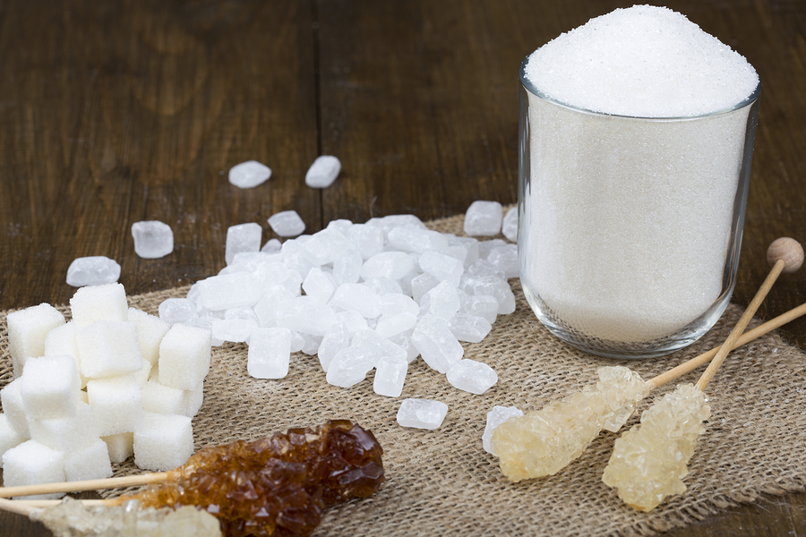 Different types of sugar on a brown wooden table. Sugar with sand in a glass. Sugar in cubes. Sugar on a stick in the form of candy. Sugar on the structural fabric.