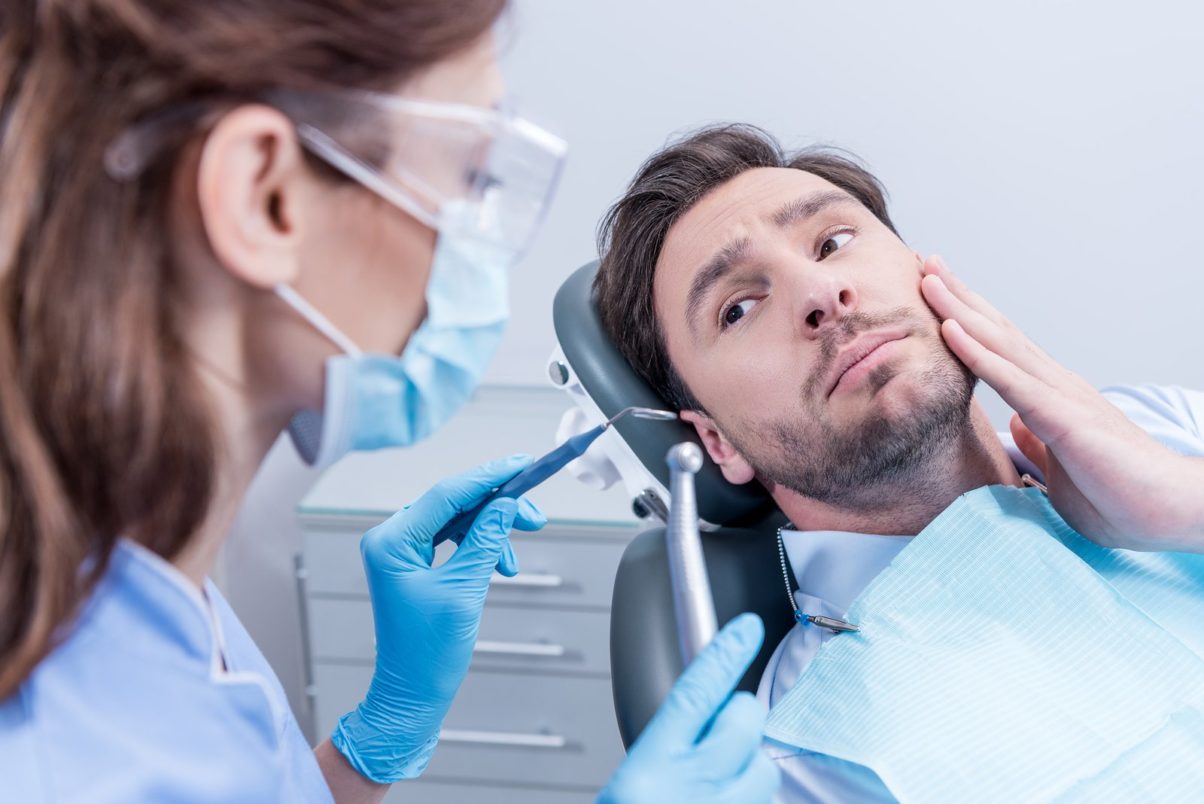 Scared Patient Looking At Dentist In Protective Mask With Dental